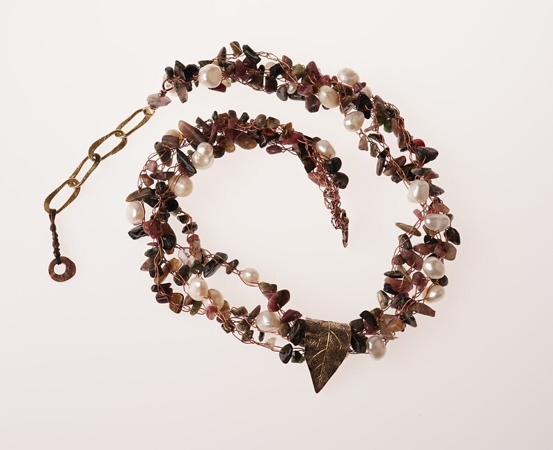 May include: A multi-strand necklace made with copper wire, small pink and green stones, and white pearls. The necklace has a leaf-shaped pendant and a brass clasp.