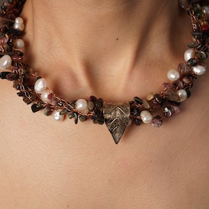 May include: A multi-strand necklace with a copper wire base and a variety of stones, including pearls, black stones, and pink stones. A leaf-shaped pendant hangs from the center of the necklace.