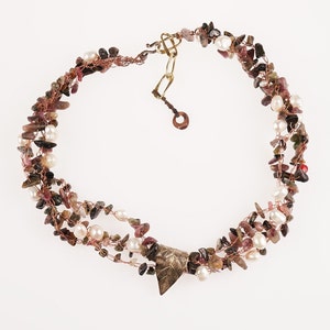 May include: A multi-strand necklace made with copper wire, small pink and green stones, and white pearls. The necklace has a triangular pendant with a leaf design.