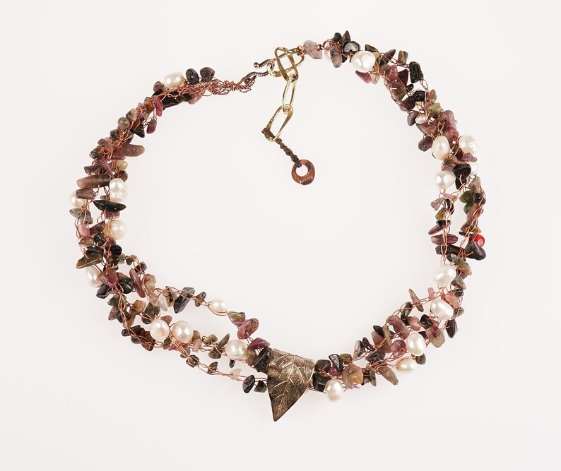 May include: A multi-strand necklace made with copper wire, small pink and green stones, and white pearls. The necklace has a triangular pendant with a leaf design.