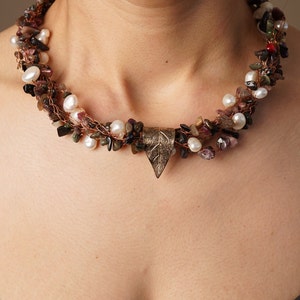 May include: A multi-strand necklace with a leaf-shaped pendant. The necklace is made of copper wire, pearls, and various small stones in shades of brown, pink, and green.