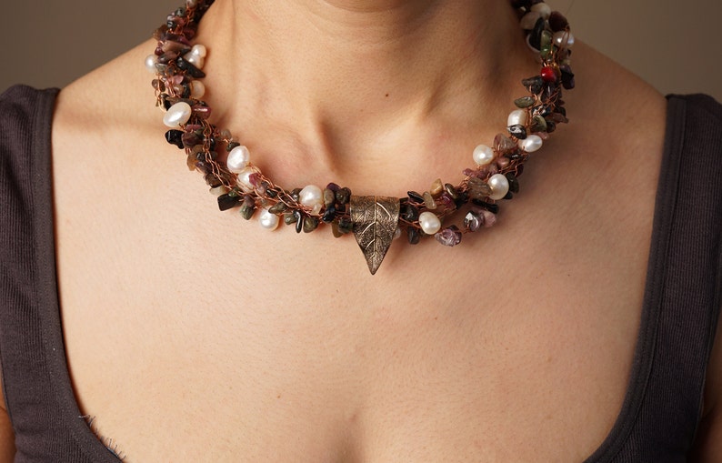 May include: A multi-strand necklace with a leaf-shaped pendant. The necklace is made of copper wire, pearls, and various small stones in shades of brown, pink, and green.