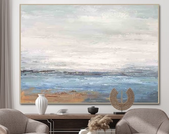 May include: Abstract painting of a seascape with a light blue ocean and a white sky. The painting is framed in a thin gold frame and is hanging on a wall above a brown wooden shelf.