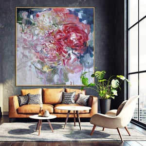 May include: Abstract painting of pink, red, and white flowers with a textured brushstroke style. The painting is displayed on a wall in a living room setting with a brown leather sofa, a coffee table, and a chair.
