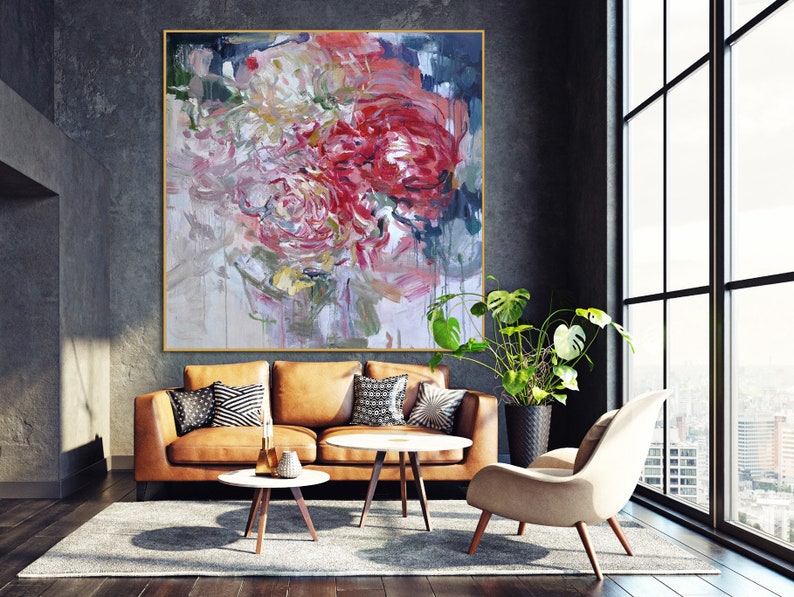 May include: Abstract painting of pink, red, and white flowers with a textured brushstroke style. The painting is displayed on a wall in a living room setting with a brown leather sofa, a coffee table, and a chair.