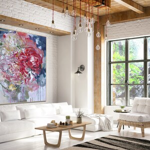 May include: A large abstract painting of pink, red, and white flowers with a blue background hangs on a white brick wall in a modern living room. The painting is above a white sofa with a wooden coffee table and a white chair.