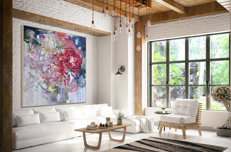 May include: A large abstract painting of pink, red, and white flowers with a blue background hangs on a white brick wall in a modern living room. The painting is above a white sofa with a wooden coffee table and a white chair.
