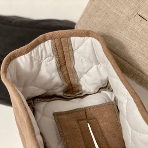 May include: Close-up of three fabric items. The primary item is a light brown, quilted fabric with a white interior. The edges are trimmed with a darker brown fabric. A black and a tan fabric item are visible in the background.