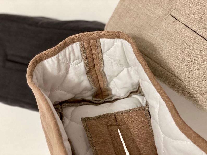 May include: Close-up of three fabric items. The primary item is a light brown, quilted fabric with a white interior. The edges are trimmed with a darker brown fabric. A black and a tan fabric item are visible in the background.
