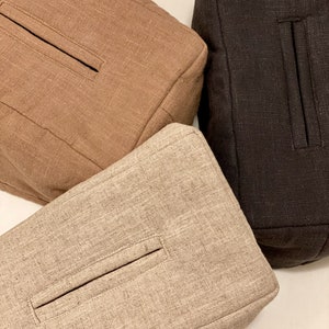 May include: Three square-shaped, textured fabric bags in varying shades of brown. The bags have a rectangular pocket detail on the front. The colors include a light tan, a medium brown, and a dark brown.