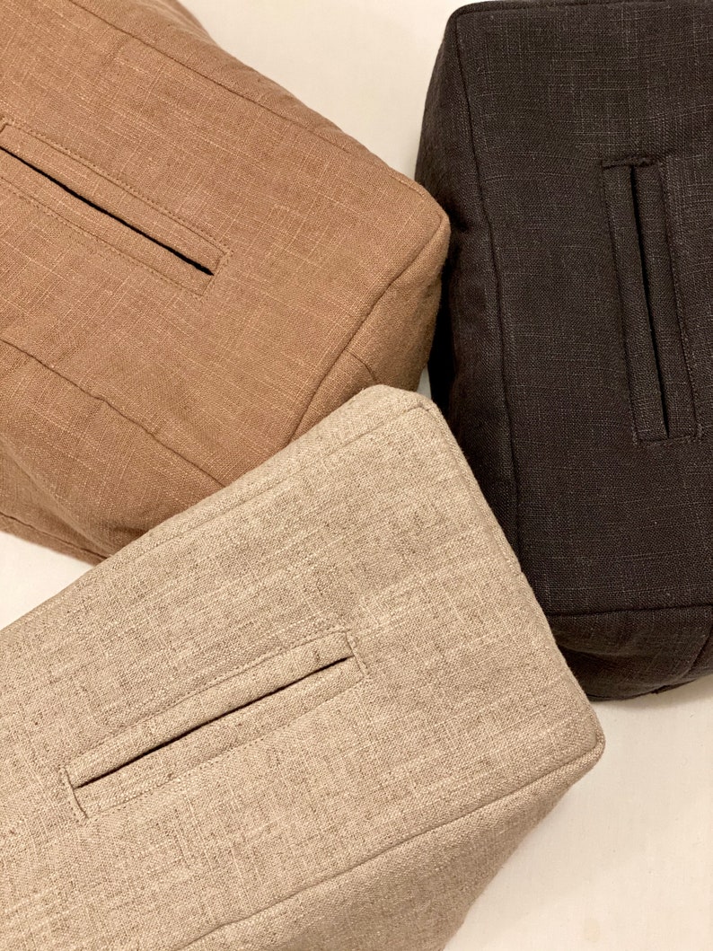 May include: Three square-shaped, textured fabric bags in varying shades of brown. The bags have a rectangular pocket detail on the front. The colors include a light tan, a medium brown, and a dark brown.