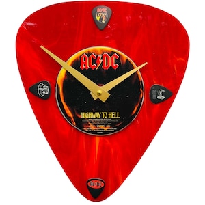 May include: Red guitar pick-shaped clock with a black and gold AC/DC "Highway to Hell" album cover in the center. The clock has four black guitar picks with band logos around the edge.