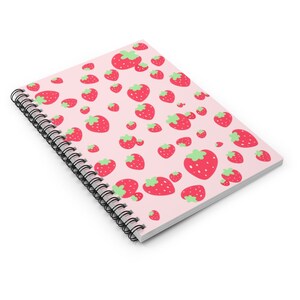 May include: A pink spiral notebook with a pattern of red strawberries. The strawberries have green leaves and are arranged in a repeating pattern.