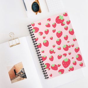 May include: A pink spiral notebook with a repeating pattern of red strawberries with green leaves.