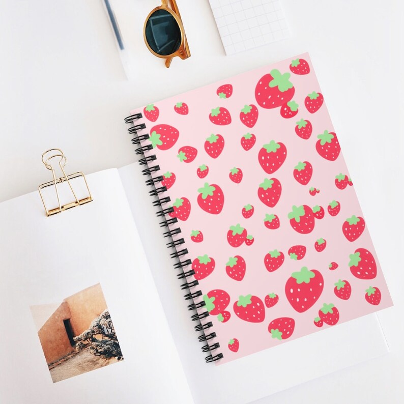 May include: A pink spiral notebook with a repeating pattern of red strawberries with green leaves.