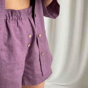May include: A purple linen button-up shirt and matching shorts set. The shirt has a relaxed fit and the shorts have an elastic waistband.
