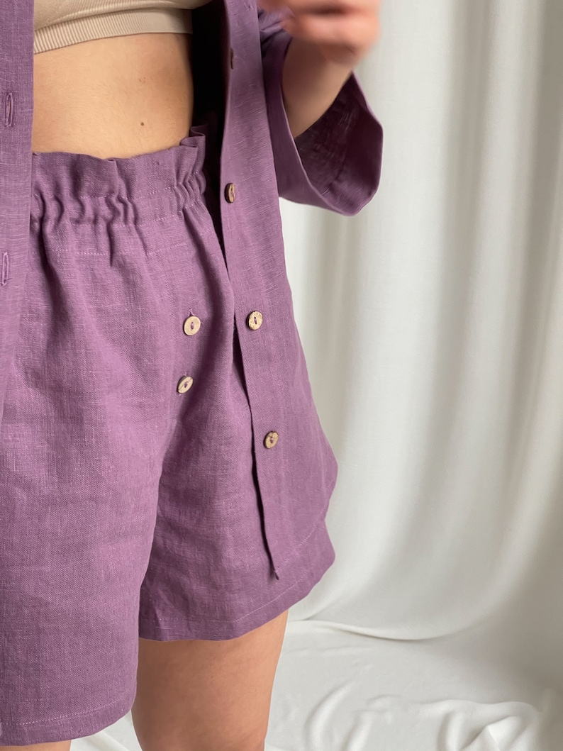 May include: A purple linen button-up shirt and matching shorts set. The shirt has a relaxed fit and the shorts have an elastic waistband.