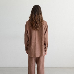 May include: A brown linen shirt and matching wide-leg pants. The long-sleeved shirt has buttoned cuffs and a classic collar. The pants have a relaxed fit. The person is wearing black sneakers.