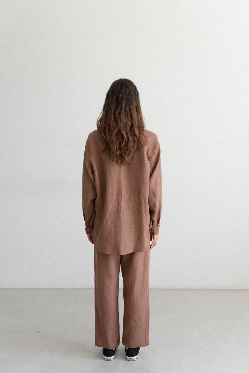 May include: A brown linen shirt and matching wide-leg pants. The long-sleeved shirt has buttoned cuffs and a classic collar. The pants have a relaxed fit. The person is wearing black sneakers.