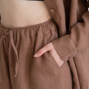 May include: A brown linen outfit, including shorts with a drawstring waist and a matching button-down shirt. The outfit is a solid, earthy tone, with a black top visible underneath the shirt. The fabric appears to be lightweight and breathable.