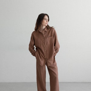 May include: A brown linen shirt and matching wide-leg pants set. The long-sleeved shirt has a button-down front and a chest pocket. The model is wearing black and white sneakers.