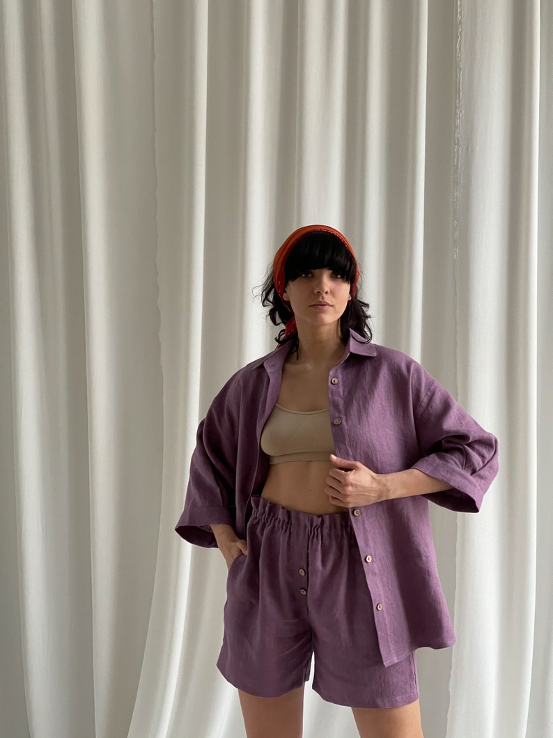 May include: A purple linen shirt and shorts set. The shirt has a button-down front and three-quarter sleeves. The shorts have an elastic waistband and a button fly.