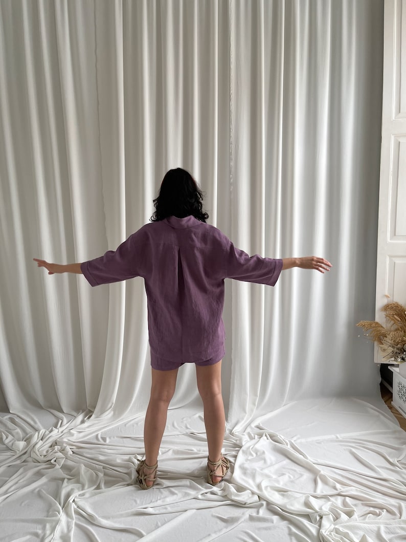May include: A woman wearing a purple linen shirt and shorts set. The outfit is loose-fitting and has a relaxed, casual style.