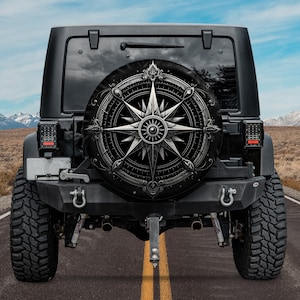 May include: A black Jeep with a spare tire cover featuring a silver compass design. The compass has a star in the center and is surrounded by a decorative border.