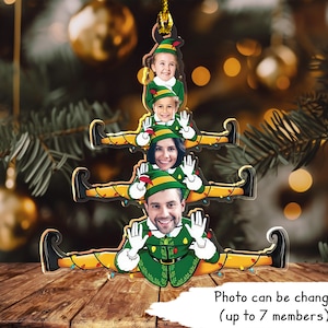 May include: A Christmas tree ornament shaped like a Christmas elf with a green hat and red shoes. The ornament is made of wood and has a string for hanging. The ornament has space for up to 7 photos to be added.