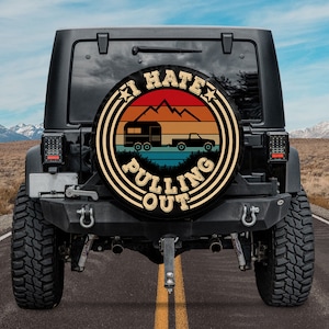 May include: A black Jeep with a spare tire cover that says "I Hate Pulling Out" with a retro sunset design and a camper and truck silhouette.