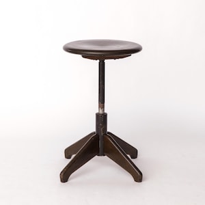 May include: A vintage, adjustable height stool with a round, dark brown seat. The stool has a dark metal stem and a tripod base. The seat is approximately 12 inches in diameter.
