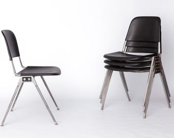 May include: Two black chairs with silver legs are shown against a white backdrop. One chair stands alone, while the other is stacked with two more chairs. The chairs have a simple, modern design.