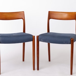Könnte beinhalten: Zwei Stühle im Mid-Century-Modern-Stil mit Holzrahmen und blau gepolsterten Sitzen. Die Stühle haben eine geschwungene Rückenlehne und konische Beine. Das Holz hat einen warmen, rötlich-braunen Farbton.