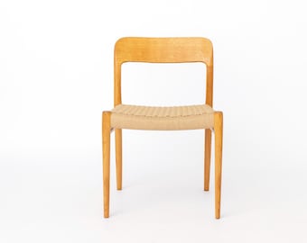 May include: A wooden chair with a light brown finish. The chair has a woven seat and a curved backrest. The legs are slender and straight. The chair is set against a white background.