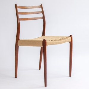 Könnte beinhalten: Ein Stuhl aus Holz im Mid-Century-Modern-Stil mit gewebter Sitzfläche. Der Stuhl hat ein dunkelbraunes Gestell mit drei horizontalen Sprossen auf der Rückseite. Der Sitz besteht aus hellbraunem, gewebtem Material. Der Stuhl hat vier abgewinkelte Beine.