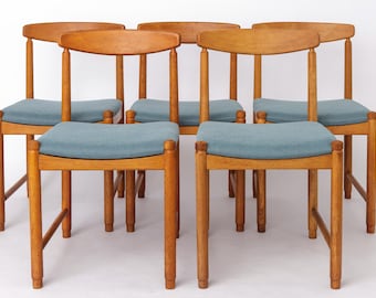 May include: Six wooden chairs with light blue upholstered seats. The chairs have a curved backrest and four legs. The wood has a natural finish. The chairs are arranged in a group, showcasing a mid-century modern design.