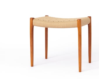 May include: A wooden stool with a woven seat and four legs. The stool is made of natural wood and has a light brown finish.
