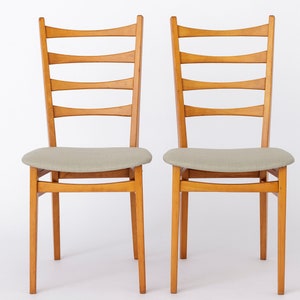 May include: Two wooden chairs with light brown wood frames and light gray fabric seats.