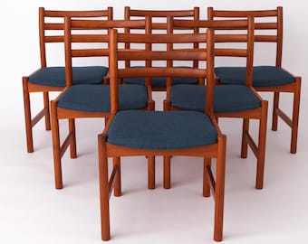 Könnte beinhalten: Sechs Holzstühle im Mid-Century-Modern-Stil. Die Stühle haben eine warme braune Oberfläche, Lattenrücken und blau gepolsterte Sitze. Die Beine sind gerade und stabil. Die Stühle sind in einer Gruppe angeordnet.