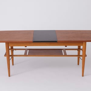 Könnte beinhalten: Ein moderner Couchtisch aus der Mitte des Jahrhunderts mit einer dunklen Holzplatte und einem schwarzen Ledereinsatz. Der Tisch hat ein Untergestell und abgeschrägte Beine.
