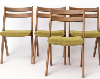 May include: Four wooden chairs with olive green upholstered seats. The chairs have a mid-century modern design, featuring a slatted back and angled legs. The wood has a warm, natural finish.