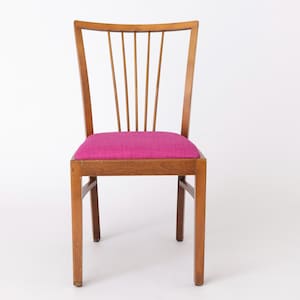 Könnte beinhalten: Ein Holzstuhl mit einem rosa gepolsterten Sitz und einer Lattenlehne.