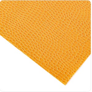 May include: Close-up of a sheet of textured, golden-yellow material. The surface has a repeating pattern of small, interconnected shapes, resembling a honeycomb or reptile skin. The material is angled, with a white background.
