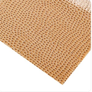 May include: Close-up of a textured, golden-brown material with a repeating honeycomb pattern. The surface has a slight sheen, suggesting a leather or faux leather appearance. The pattern is consistent across the visible area.