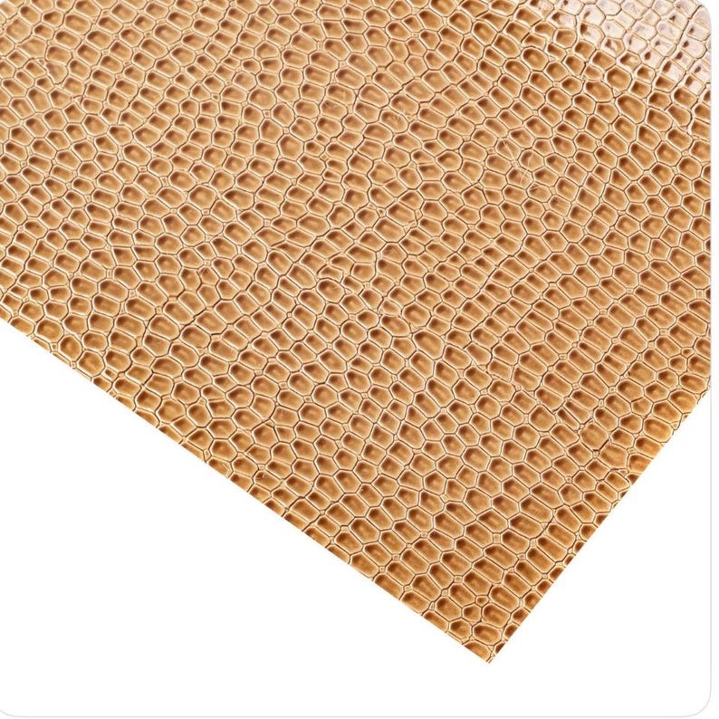 May include: Close-up of a textured, golden-brown material with a repeating honeycomb pattern. The surface has a slight sheen, suggesting a leather or faux leather appearance. The pattern is consistent across the visible area.