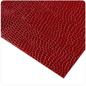 May include: Close-up of a sheet of red faux leather with a textured, scale-like pattern. The material has a glossy finish and a slight sheen, with a repeating hexagonal design. The color is a deep, rich red.