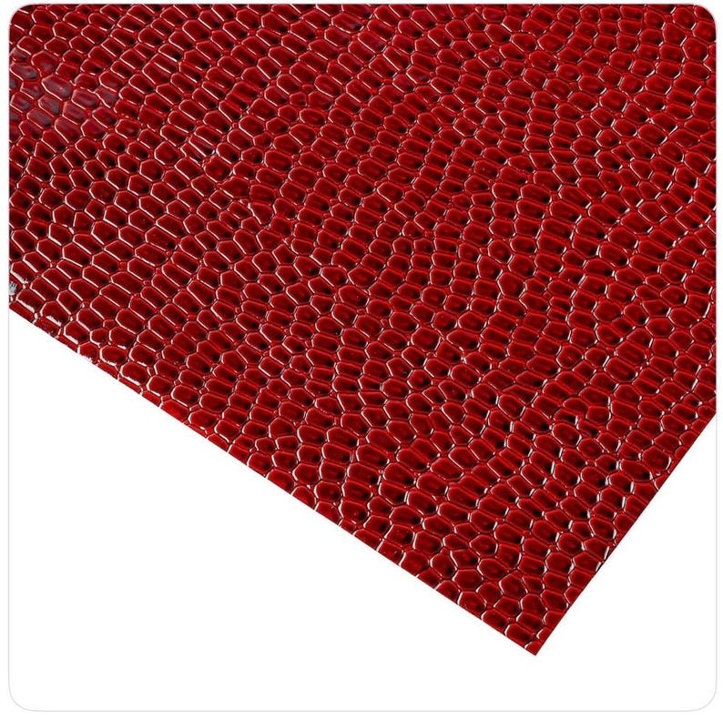 May include: Close-up of a sheet of red faux leather with a textured, scale-like pattern. The material has a glossy finish and a slight sheen, with a repeating hexagonal design. The color is a deep, rich red.