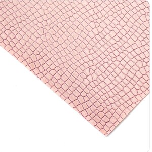 May include: A close-up of a sheet of pink faux leather with a crocodile skin texture. The pattern consists of small, irregular, interconnected shapes, creating a realistic reptile skin effect. The material is angled against a white background.
