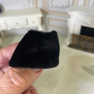 May include: A miniature black skirt made of a soft, fuzzy, velvet-like fabric. The garment features a simple, flared silhouette with a straight hemline and a dense, uniform texture that covers the entire surface of the small piece of clothing.