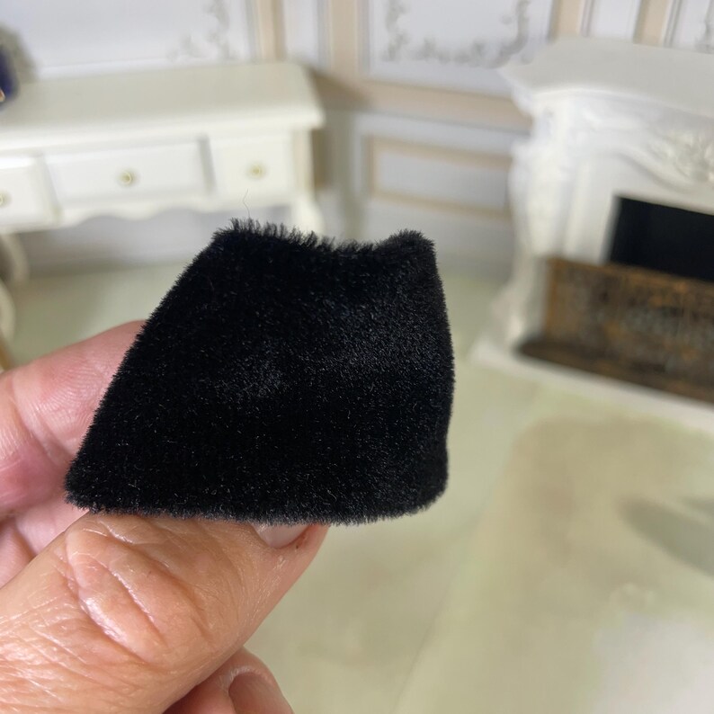 May include: A miniature black skirt made of a soft, fuzzy, velvet-like fabric. The garment features a simple, flared silhouette with a straight hemline and a dense, uniform texture that covers the entire surface of the small piece of clothing.
